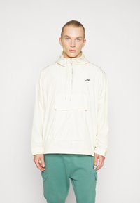 Nike letvægt cremet pullover-jakke med hætte, justerbar snor, stort frontlomme og subtilt sort logo på brystet.