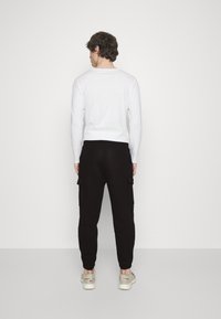 Witte lange mouwenshirt, zwarte cargobroek met zijzakken en lichtgekleurde sneakers. Eenvoudig ontwerp met een comfortabele pasvorm.