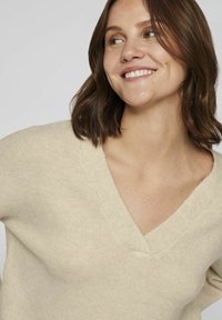 Beige v-neck sweater with a soft texture. The knit features a relaxed fit and minimal detailing, enhancing its versatile appeal.