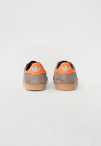 Pruunist nahast treenijad siniste külgaktsentidega, oranžide kannaosadega ja tekstuursete kummitaldadega; sisaldavad Adidas logo kanna peal.