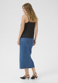 Débardeur en satin noir avec des fines bretelles, associé à une longue jupe en denim bleu. Chaussures : escarpins noirs à talons ouverts avec un bout pointu.