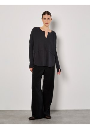 Haut en maille grise à col en V et manches longues, associé à un pantalon noir taille haute à jambe large et des chaussures plates.