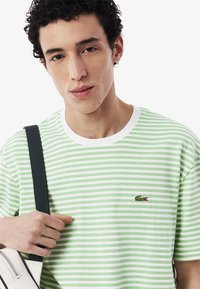 Camiseta a rayas en verde claro y blanco, con cuello redondo, mangas cortas y un pequeño logotipo bordado en el pecho.