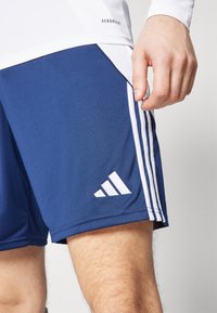 Blaue Sportshorts aus dehnbarem Stoff, mit drei weißen Streifen an der Seite und einem weißen Adidas-Logo am unteren linken Bein.