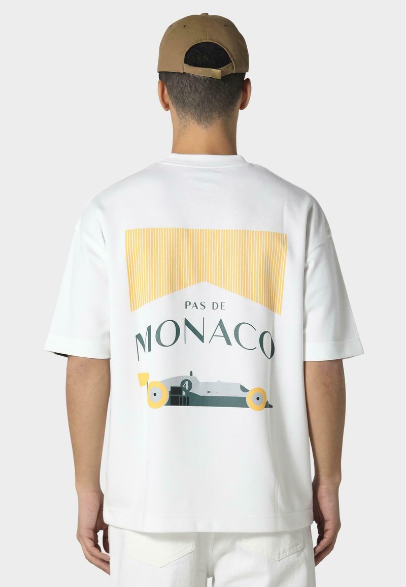 Hvid kortærmet t-shirt med "PAS DE MONACO" grafik, gule og grønne striber, og en racerbilsillustration på ryggen.