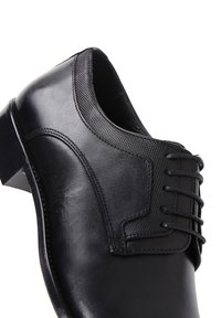 Chaussure de ville en cuir noir avec une finition lisse, des détails de couture élaborés et un accent en tissu texturé près des lacets.