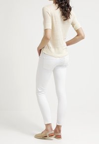 Jasno beżowa bluzka z krótkim rękawem, białe obcisłe dżinsy i beżowe espadryle, widok z tyłu. Gładka faktura, dopasowany krój, casualowy wygląd.