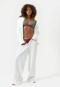 Groene kanten bralette met bordeauxrode details, gecombineerd met bijpassende bordeauxrode onderbroek. Het model draagt een oversized witte blazer en wijde witte broek.