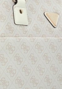 Bolso de mano blanco con textura que presenta un patrón en relieve, una etiqueta en marrón claro y una placa de logo triangular en color rosa dorado.