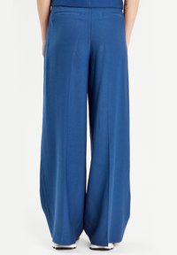 Pantalon à jambes larges en tissu bleu vif uni. Il présente une taille haute, deux poches arrière et une finition lisse et ajustée.