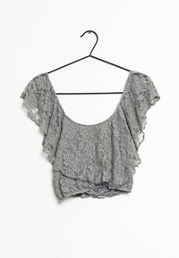 Grå spetsblus med fjärilsärmar, med en rundad halsringning och en knutdetalj framtill, hängande på en svart galge.