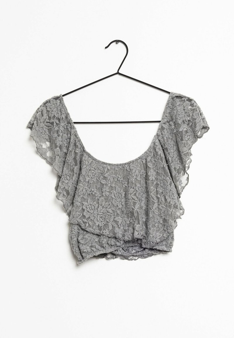 Grå spetsblus med fjärilsärmar, med en rundad halsringning och en knutdetalj framtill, hängande på en svart galge.