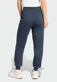 Námornícke modré tepláky s elastickým pásom a úzkymi členkami, s jemnou textúrou a bočnými vreckami, v kombinácii s bielymi teniskami.