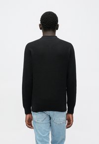 Camisola preta de malha com padrão texturizado, decote redondo e mangas compridas. Apresentada com jeans azul claro.