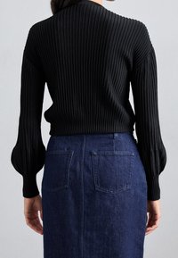 Svart ribbad tröja med långa puffärmar, i kombination med en mörk denimkjol som har två bakfickor och rak skärning.