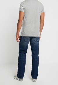 Grå kortärmad t-shirt för män, blå denimjeans med blekta detaljer och vita sneakers. Jeansen har en något avslappnad passform och bakfickor.
