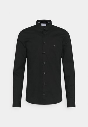 Schwarzes Herrenhemd mit langen Ärmeln, Mandarin-Kragen, Knopfleiste vorne und kleinem weißen "ck"-Logo auf der linken Brust.