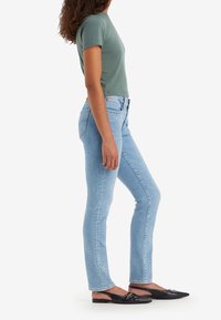 Ljusblå jeans med slim fit, parat med en grön topp med kort ärm och svarta spetsiga flats. Enkelt mönster, medelhög midja.