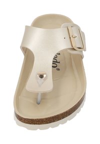 Light beige sandal with a T-bar design, featuring a metallic buckle and stud detail. The sole is textured with a cork accent.