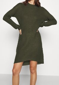 Abito maglione in verde oliva, con una vestibilità comoda, maniche lunghe, texture a coste e tasche laterali, con un orlo leggermente curvo.