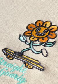 Broderat mönster med en leende gul blomma på en skateboard, med svarta konturer, gröna blad och turkosa texter som säger "Straight Gnarly."