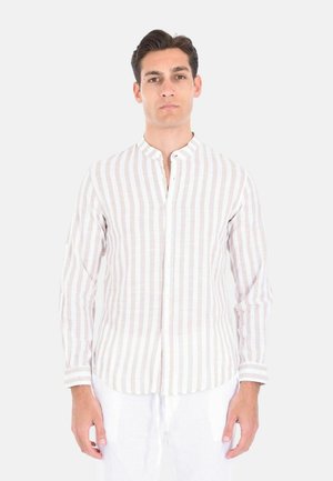 Uomo che indossa una camicia a righe verticali beige e bianca a maniche lunghe con colletto alla coreana, in piedi davanti a uno sfondo semplice.