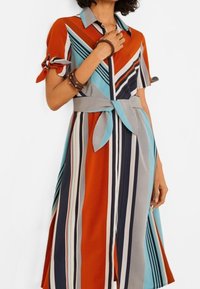 Robe à rayures rouge, bleue et grise avec manches courtes, fermeture boutonnée sur le devant, col et ceinture en tissu à la taille. Matière texturée.