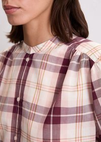 Chemise à carreaux en coton doux ; présente un motif à carreaux violet, rose et beige, une fermeture à boutons et un col montant avec des manches légèrement bouffantes.