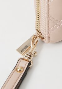 Portafoglio in faux leather rosa chiaro con zip dorata, design trapuntato e chiusura a moschettone dorato con un'etichetta rettangolare incisa con la scritta "GUESS."