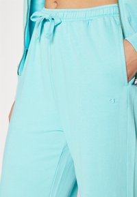 Ανοιχτό μπλε παντελόνι φόρμας με ελαστική μέση και κορδόνι. Διαθέτει τσέπες και ένα μικρό κεντημένο λογότυπο στο μηρό. Υφασμάτινη από βαμβάκι.