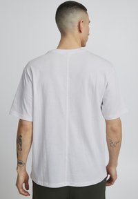 Witte t-shirt met korte mouwen en ronde hals, gemaakt van gestructureerde stof en met een rechte zoom. Zichtbare tatoeages op de rechterarm.