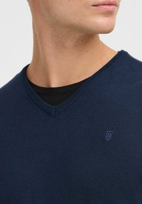 Granatowy sweter w serek, wykonany z gładkiego dzianiny, z delikatnym logo na piersi i prążkowanym dekoltem.