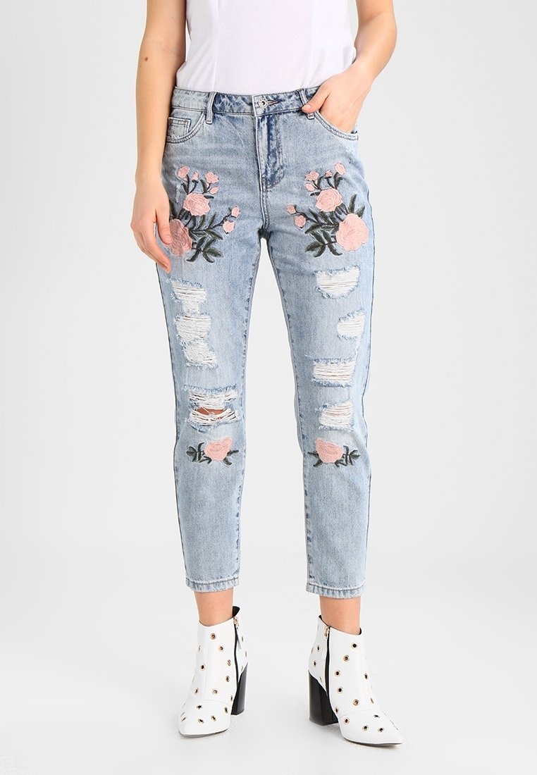 Světle modré potrhané džíny s růžovou květinovou výšivkou na přední straně, s roztrhanými detaily a zúženým střihem nohavic.