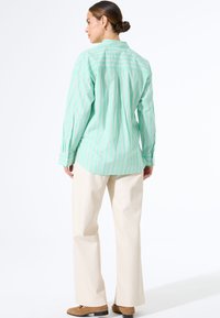 Lichtgroen gestreept shirt met lange mouwen, button-down kraag en een relaxed fit. Gecombineerd met crèmekleurige wijde broek en bruine schoenen.