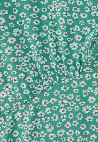 Tela verde con pequeñas flores blancas, además de acentos morados y marrones. Presenta una textura fruncida y un acabado suave.
