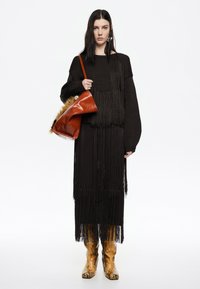 Sweater negro con flecos y falda midi, junto con botas metálicas doradas de estampado de serpiente. También se muestra un bolso de cuero marrón con borde de piel.