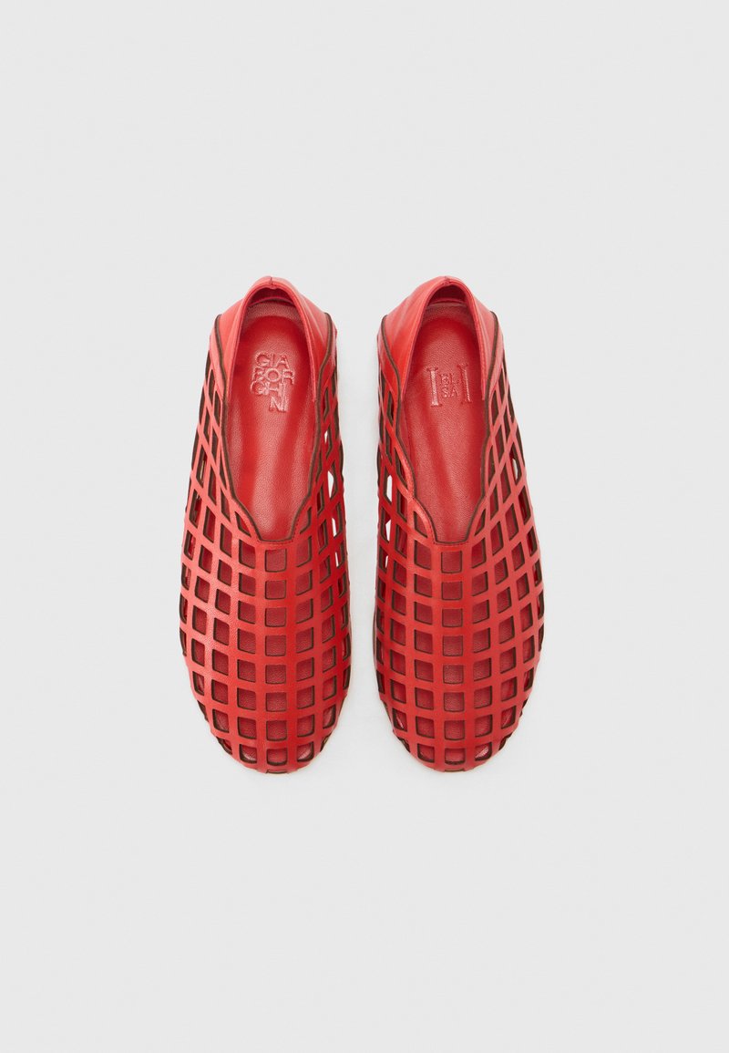 Zapatos rojos sin cordones con un patrón de cuadrícula, hechos de material flexible, con un forro interior suave y un diseño de punta redondeada.