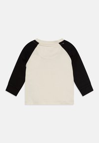 Langermige raglan shirt met een crème lichaam en zwarte mouwen, gemaakt van katoen, met een ronde hals en contrasterende stiksels langs de schoudernaad.