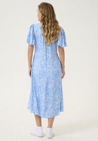 Abito floreale azzurro chiaro con maniche a puff corte, orlo a lunghezza ginocchio e vestibilità rilassata, abbinato a sneakers bianche alte.