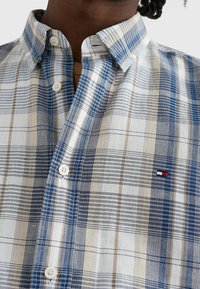 Camisa de manga corta a cuadros en azul, beige y blanco. Cuenta con cuello abotonado y sutil detalle de logo en el pecho. Material de algodón.