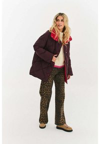 Bordowa kurtka puchowa z czerwonym kołnierzem, beżowe i czarne spodnie w panterkę oraz beżowe buty na sznurowadła. Charakteryzuje się pikowaną strukturą i luźnym fasonem.