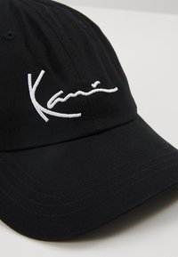 Svart baseballkeps i bomull med krökt skärm, prydd med vitt broderat signaturlogga på framsidan.