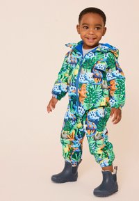 Colorful children's waterproof jumpsuit featuring a dinosaur and foliage pattern, with a blue zipper and elastic cuffs. Black rubber boots.