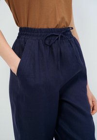 Marina blå linbyxor med elastisk midja och dragsko, med sidofickor och avslappnad passform. Materialet har en lätt struktur.