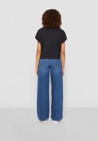 Schwarzes, kurz geschnittenes T-Shirt mit aufgerollten Ärmeln, kombiniert mit weiten blauen Jeans aus Denim. Die Jeans verfügen über ein klassisches Fünf-Taschen-Design.