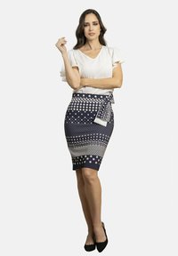 Falda lápiz azul marino con lunares blancos y un lazo en la cintura, combinada con una blusa blanca de manga corta y tacones negros.