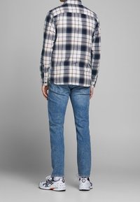 Geruite shirt in blauw, wit en oranje, met lange mouwen en een kraag. Gepaard met lichtblauwe spijkerbroek en witte sportschoenen.