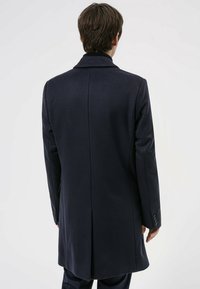 Abrigo azul marino con ajuste entallado, mangas largas y solapa con muesca. Presenta una textura suave, abertura trasera y puños abotonados.