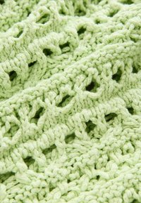 Tissu en dentelle tricoté de couleur vert pastel doux, présentant un motif texturé avec des ouvertures et des coutures complexes. Apparence légère et délicate.
