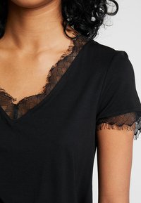 T-shirt noir avec un col en V, présentant une délicate bordure en dentelle noire le long du col et des manches courtes, fabriqué dans un tissu doux.